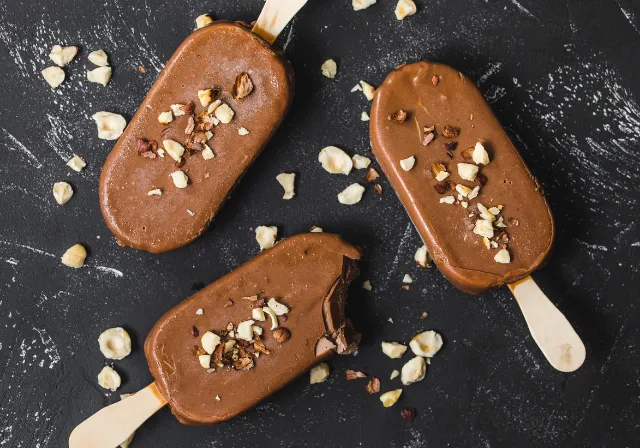 Three chocolate-coated frozen desserts topped with chopped nuts and cocoa nibs.