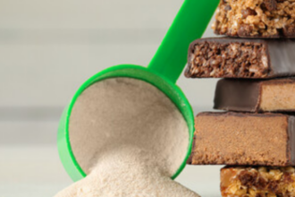 Green scoop filled with protein powder beside a stack of chocolate-coated protein bars.