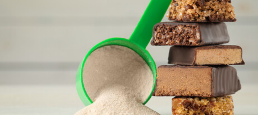 Green scoop filled with protein powder beside a stack of chocolate-coated protein bars.
