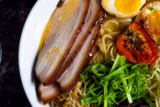 Bowl of pork ramen topped with sliced pork belly, soft-boiled eggs, spring onion, bean sprouts and roasted tomato, served with crème brûlée.