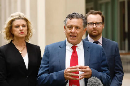 Richard Forbes speaking to the media with two colleagues standing behind him.