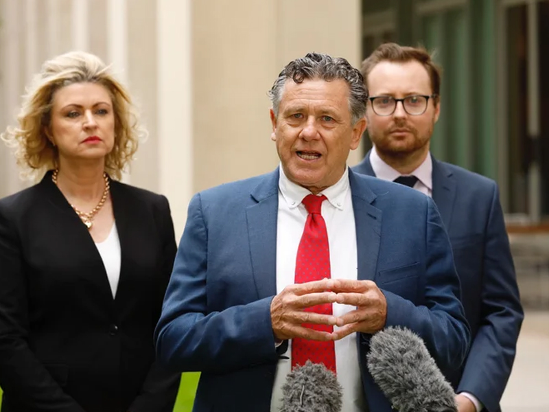 Richard Forbes speaking to the media with two colleagues standing behind him.