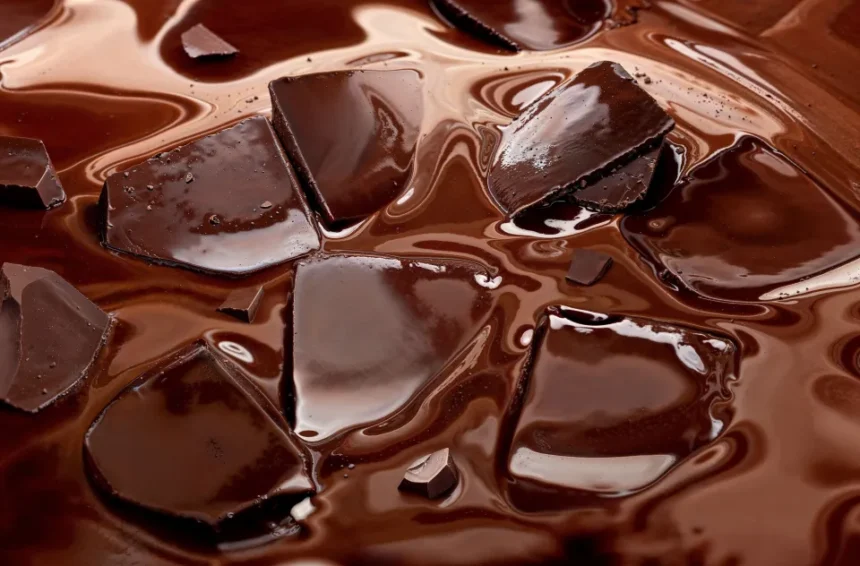 Broken dark chocolate pieces partially submerged in glossy melted chocolate.