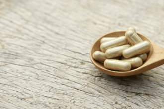 Nutritional supplement capsules displayed in a wooden spoon beside green leaves.