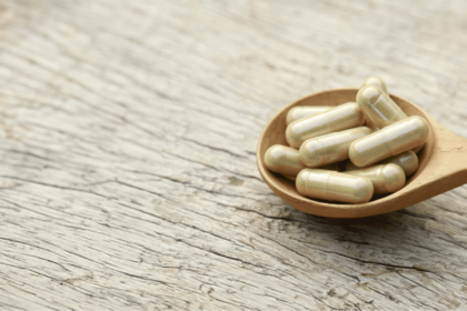 Nutritional supplement capsules displayed in a wooden spoon beside green leaves.