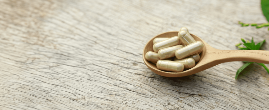 Nutritional supplement capsules displayed in a wooden spoon beside green leaves.