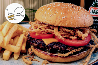 Busy Bee Cafe burger topped with cheese, tomato and crispy onions, served with hot chips and a bottle of Jarritos Mexican Cola.