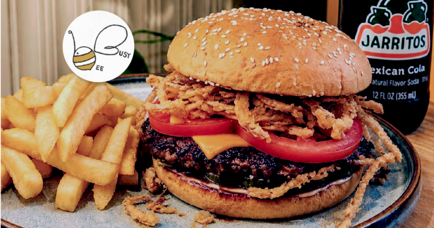 Busy Bee Cafe burger topped with cheese, tomato and crispy onions, served with hot chips and a bottle of Jarritos Mexican Cola.