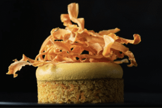 Individual Gold carrot cake with a smooth golden topping and crisp carrot ribbons against a dark background.