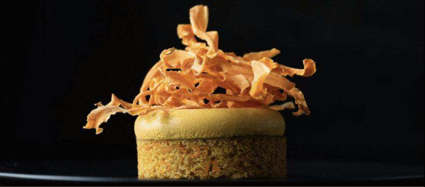 Individual Gold carrot cake with a smooth golden topping and crisp carrot ribbons against a dark background.