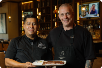 Andy Hearnden and Chef from Fleming’s Prime Steakhouse holding a plated Australian Wagyu steak inside a North American restaurant.