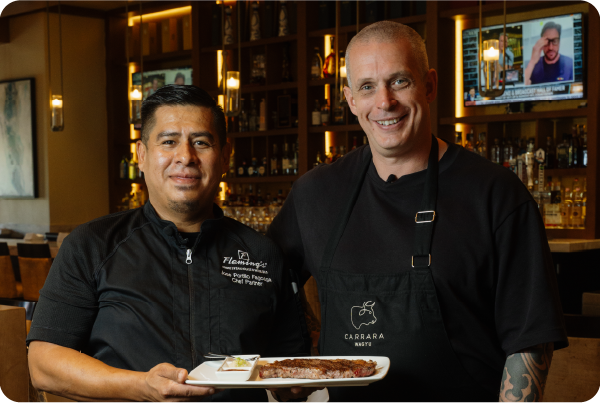Andy Hearnden and Chef from Fleming’s Prime Steakhouse holding a plated Australian Wagyu steak inside a North American restaurant.