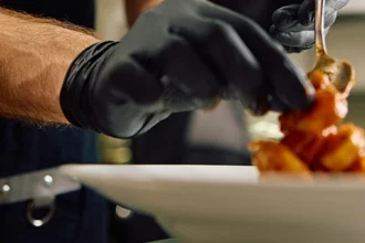 Chef plating a dish coated in a glossy sweet and spicy sauce in a commercial kitchen.
