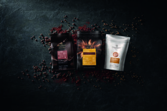 Three Callebaut products displayed with chocolate callets, cocoa powder and Crispearls on a dark textured background.