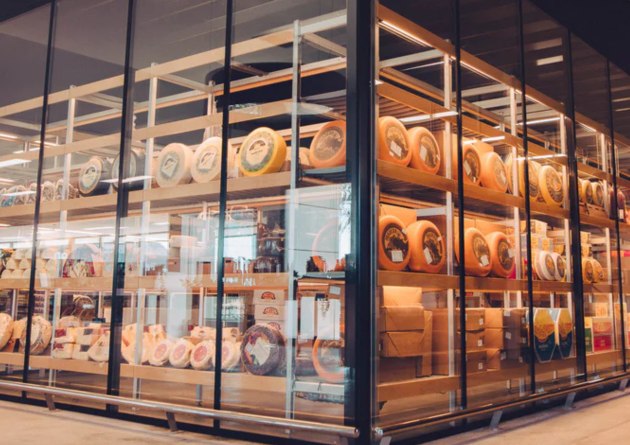 Wheels and blocks of specialty cheese displayed on shelves behind glass.