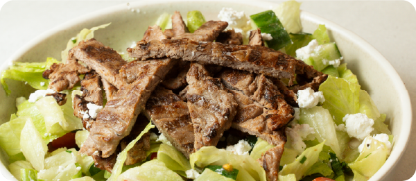 Piccolo Me salad topped with sliced sous vide steak, lettuce, cucumber and feta.