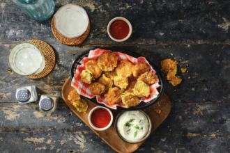 Crispy fried pickle chips served with creamy dill dip and red dipping sauce on a rustic bar table.