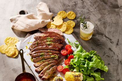 Sliced skirt steak with cowboy butter, grilled corn, lettuce, tomatoes and corn chips on a sharing board.