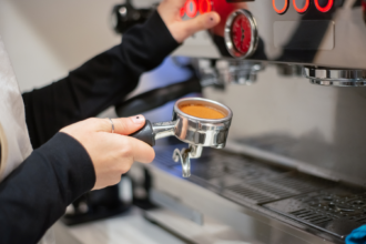Barista holding a portafilter filled with ground coffee beneath a commercial espresso machine.
