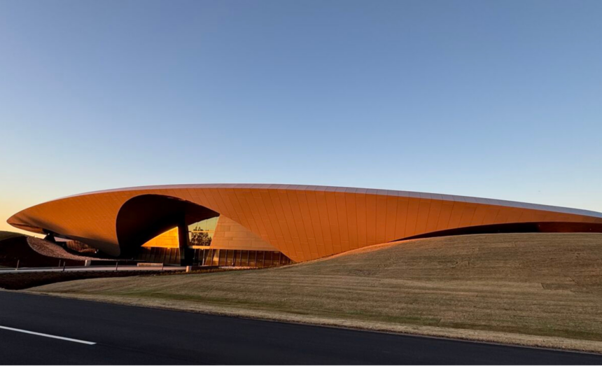 Modern poultry processing facility with a sweeping orange roof and landscaped grounds
