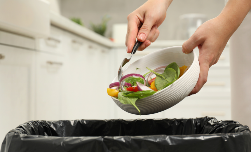 Person scraping leftover salad from a bowl into a lined rubbish bin.