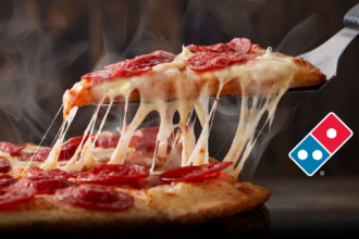 Slice of pepperoni pizza lifted with melted cheese stretching from the remaining pizza, alongside the Domino’s logo.