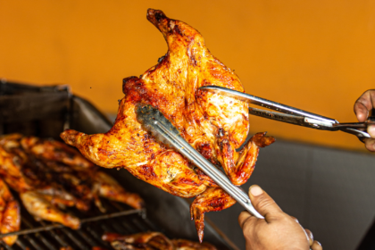 Whole roasted chicken held with metal tongs while being cut with kitchen shears.
