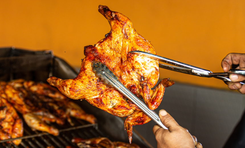 Whole roasted chicken held with metal tongs while being cut with kitchen shears.