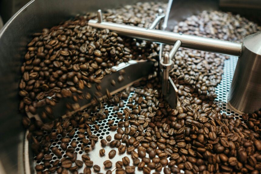 Freshly roasted coffee beans being stirred by rotating metal arms inside an industrial coffee roasting machine's cooling tray.